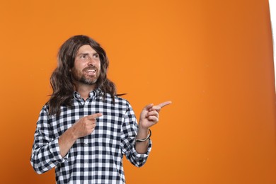 Photo of Hippie man pointing at something on orange background, space for text