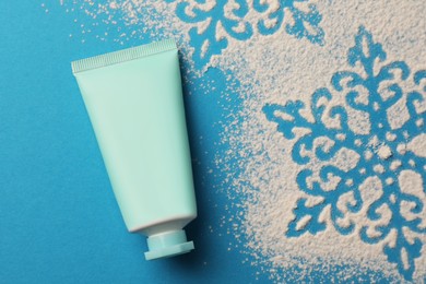 Photo of Tube of hand cream and snowflakes on light blue background, top view. Winter skin care