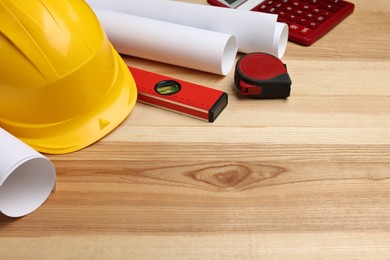 Construction drawings, safety hat, calculator, tape measure and bubble level on wooden table. Space for text