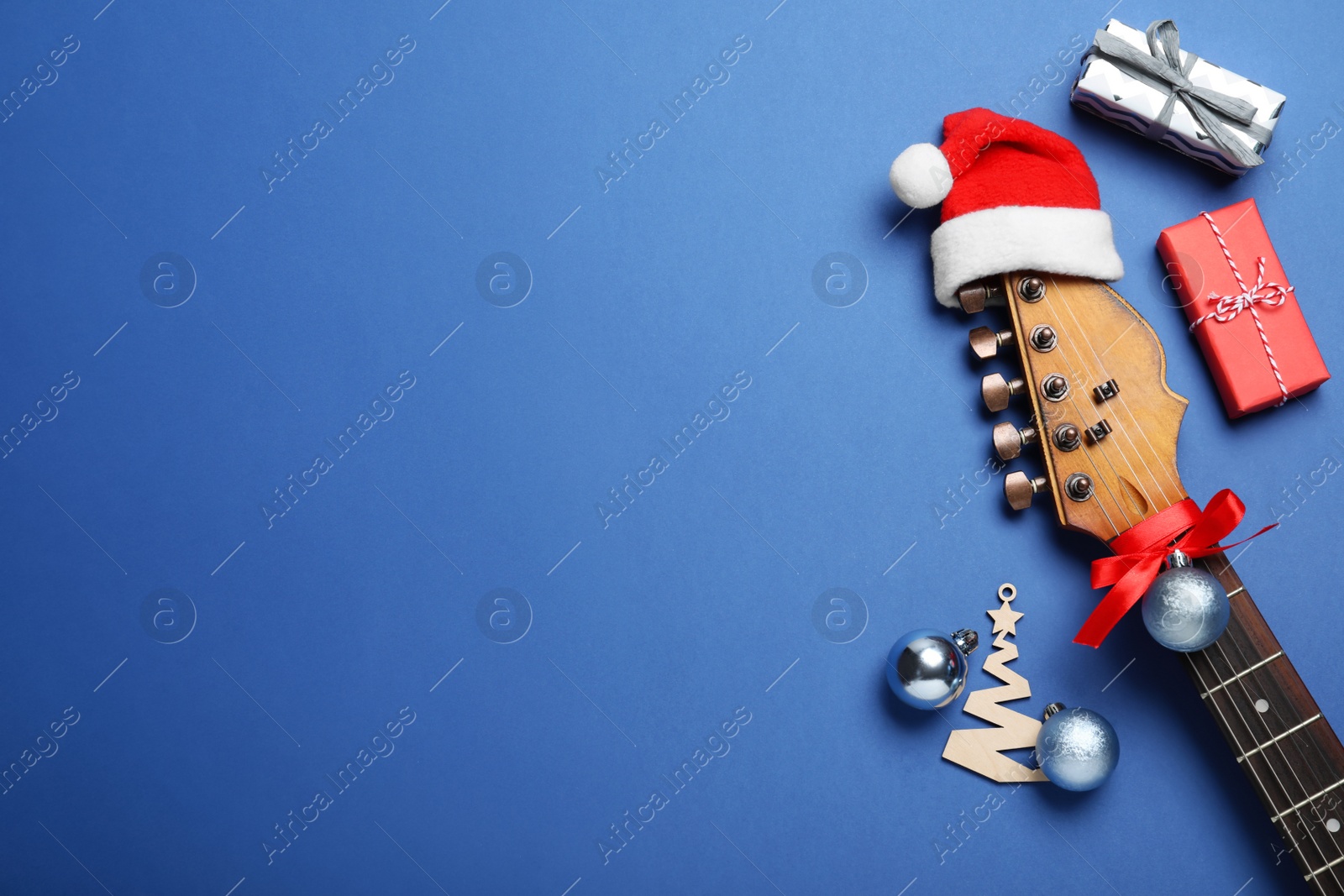 Photo of Flat lay composition with guitar and Santa hat on blue background, space for text. Christmas music