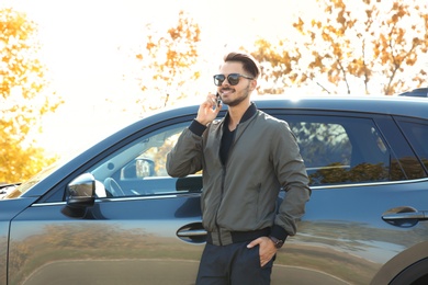 Young man talking on phone near modern car, outdoors