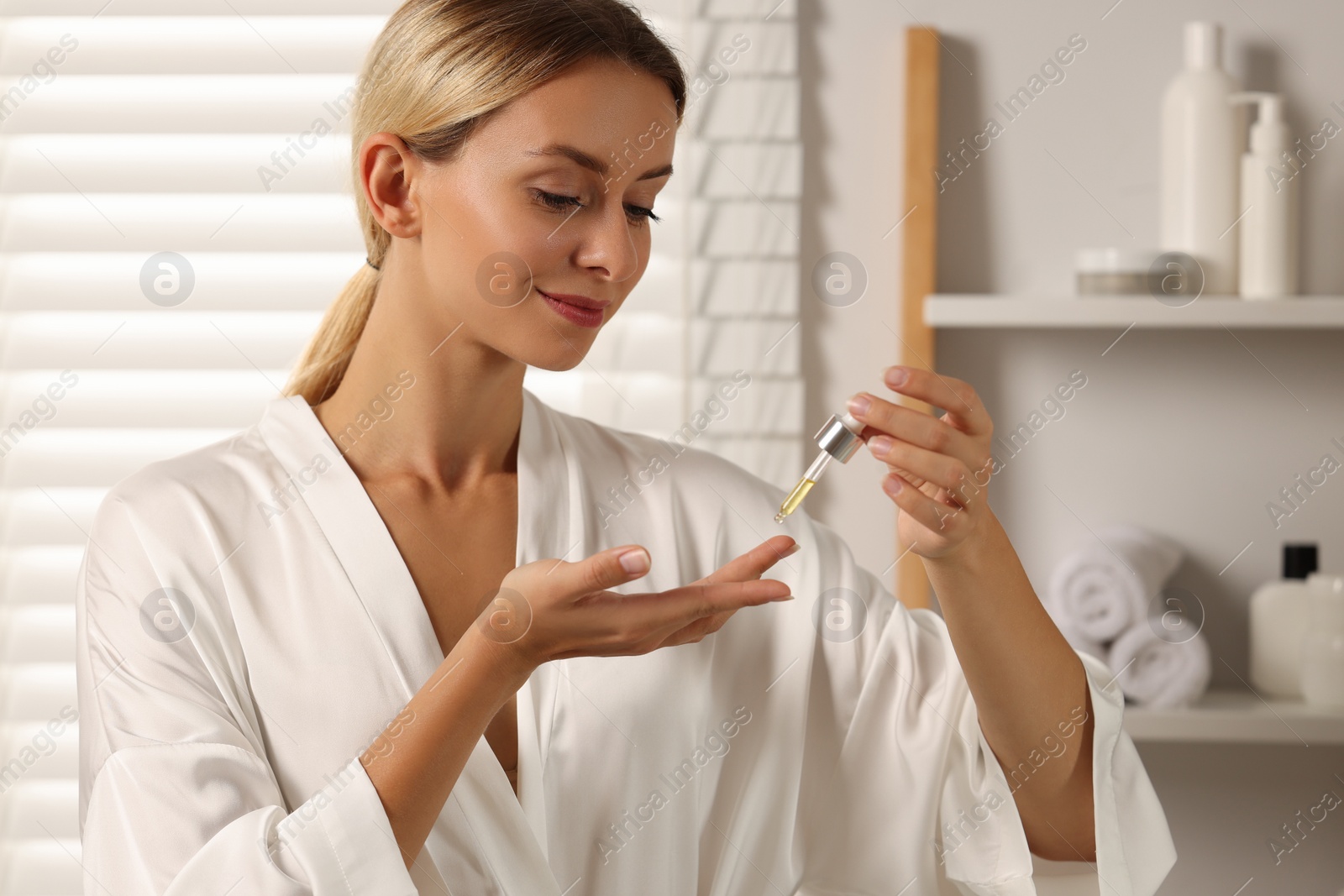 Photo of Beautiful woman applying cosmetic serum onto her hand in bathroom