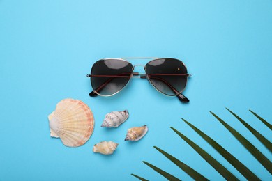 Stylish sunglasses and seashells on light blue background, flat lay