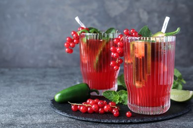 Photo of Glasses of spicy red currant cocktail with jalapeno and mint on grey table. Space for text