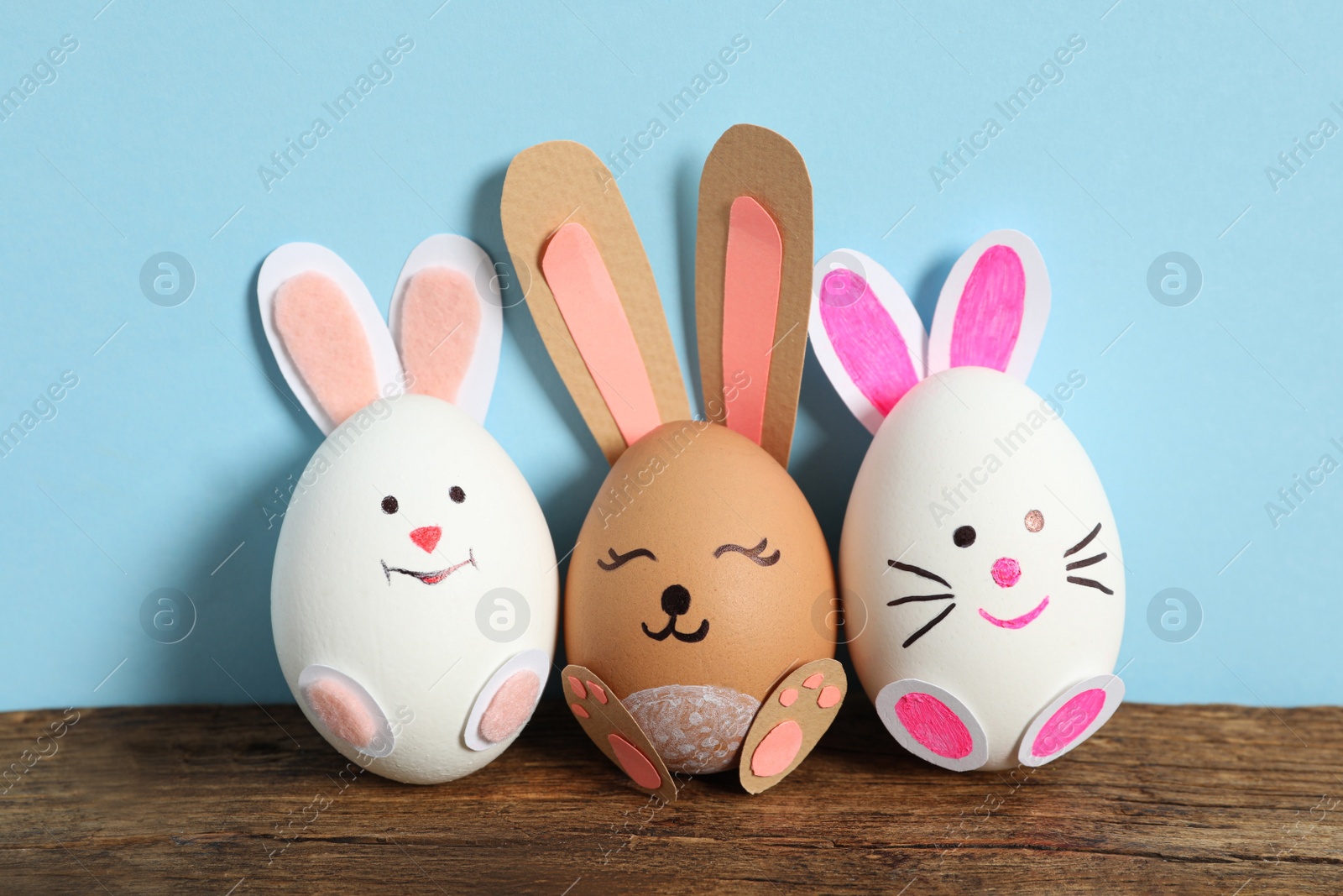 Photo of Eggs as cute bunnies on wooden table against light blue background. Easter celebration