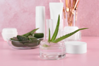 Photo of Jar of natural gel and aloe vera leaves on pink table