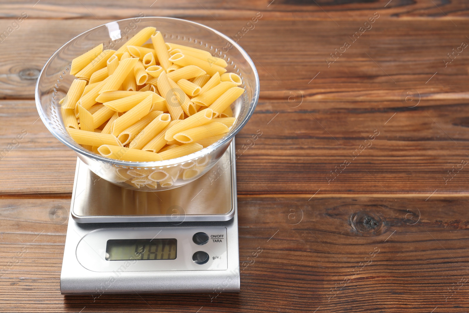 Photo of Kitchen scale with bowl of pasta on wooden table. Space for text