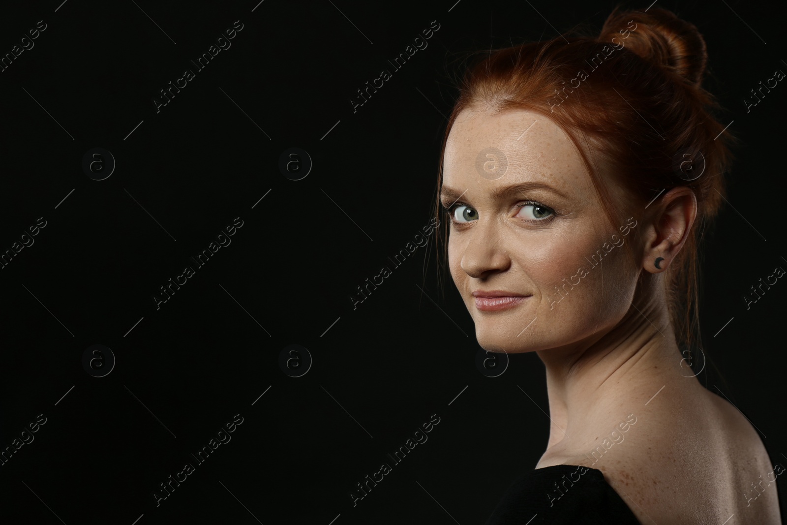 Photo of Candid portrait of happy red haired woman with charming smile on dark background, space for text