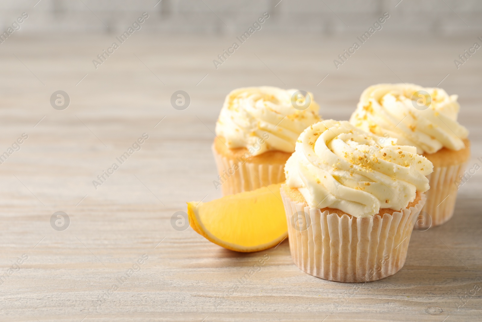 Photo of Tasty cupcakes with cream, zest and lemon slice on light wooden table. Space for text