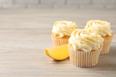 Photo of Tasty cupcakes with cream, zest and lemon slice on light wooden table. Space for text