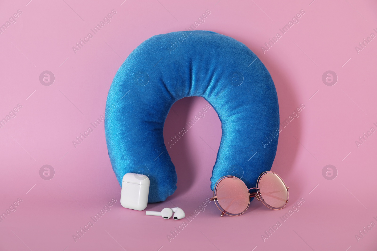 Photo of Light blue travel pillow, sunglasses and earphones on pink background