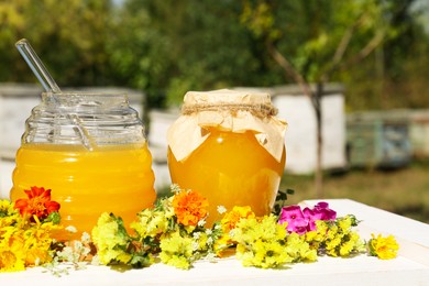 Delicious fresh honey and beautiful flowers on white wooden table in apiary