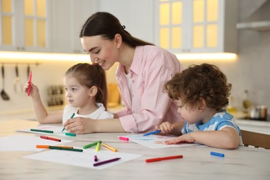 Photo of Mother and her little children drawing with colorful markers at table in kitchen