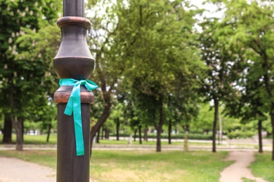 Photo of Teal awareness ribbon tied on lamppost in park, space for text