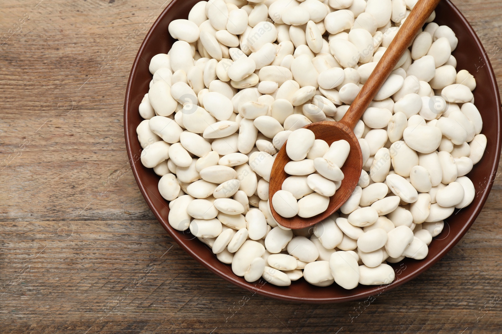 Photo of Raw white beans and spoon in bowl on wooden table, top view