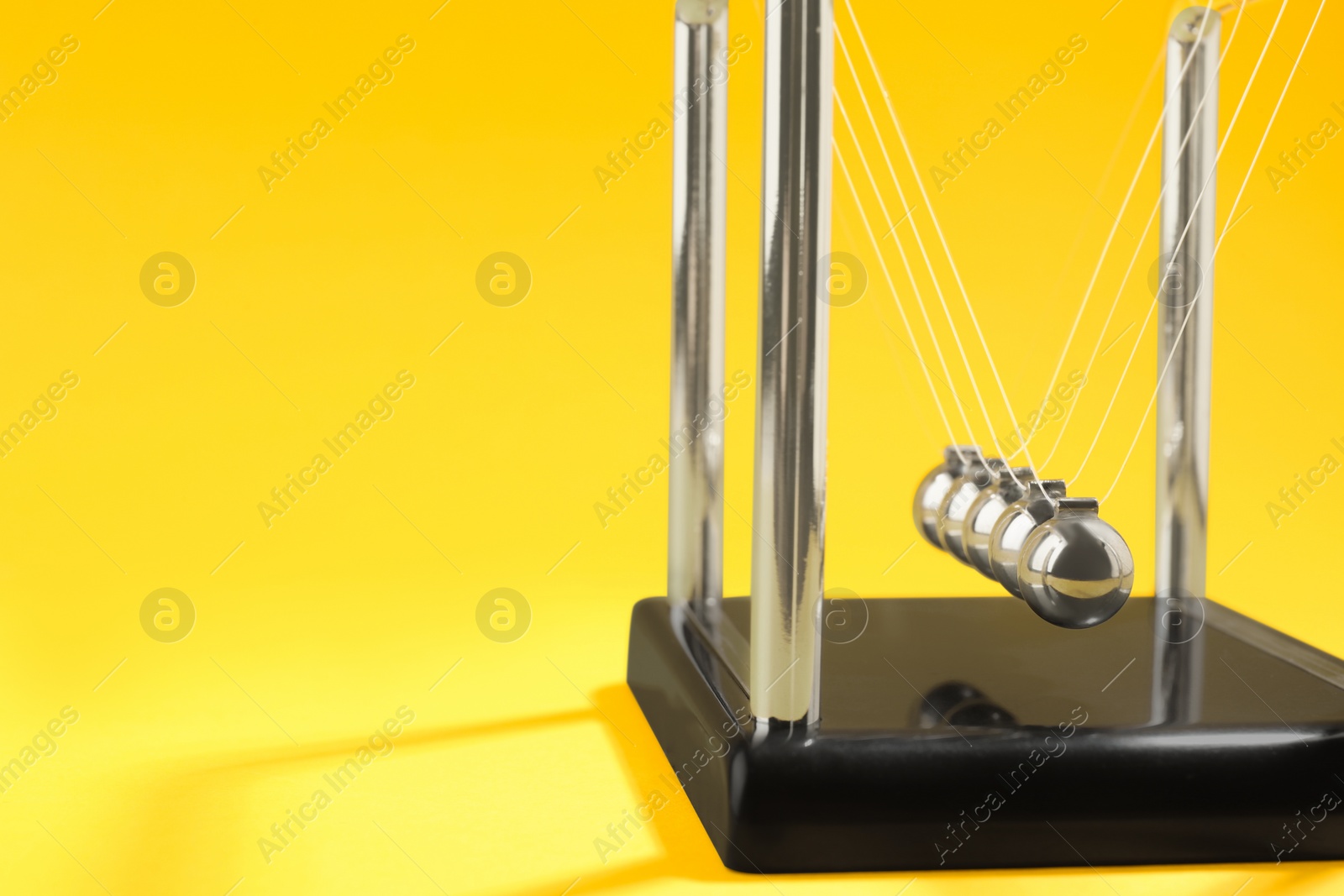 Photo of Newton's cradle on yellow background, space for text. Physics law of energy conservation