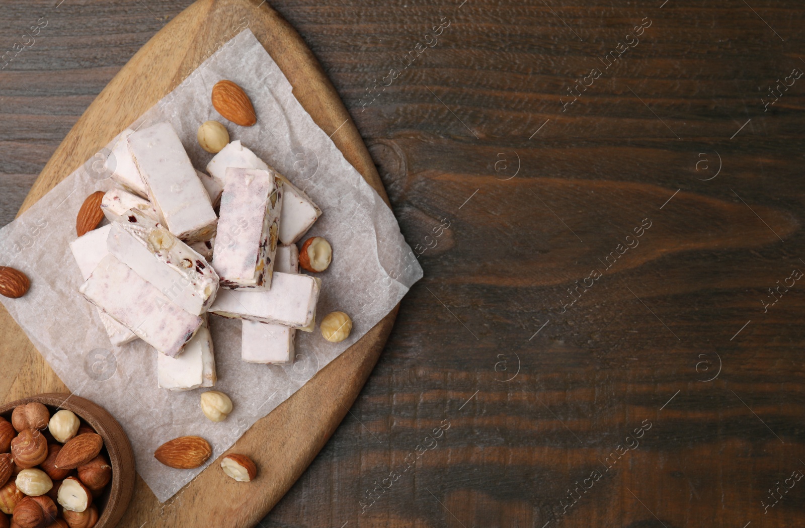 Photo of Pieces of delicious nutty nougat, hazelnuts and almonds on wooden table, top view. Space for text