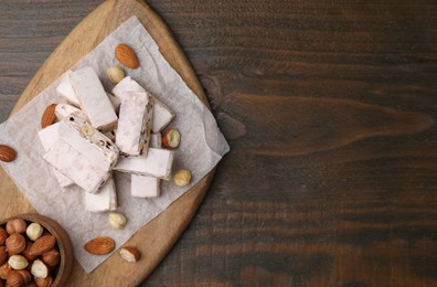 Photo of Pieces of delicious nutty nougat, hazelnuts and almonds on wooden table, top view. Space for text