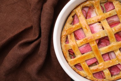 Baking dish with tasty apple pie on brown cloth, top view. Space for text