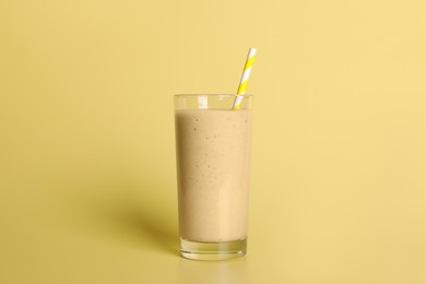 Photo of Glass of tasty smoothie with straw on pale yellow background