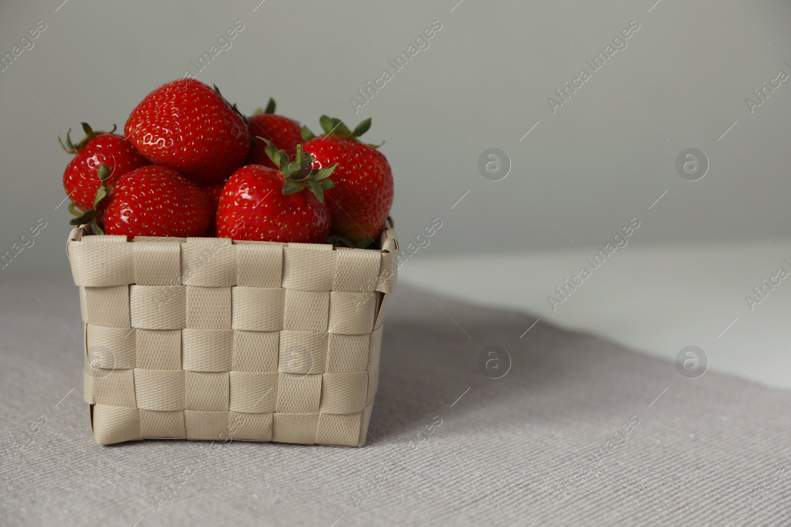 Photo of Fresh juicy strawberries in wicker basket on table, closeup. Space for text