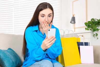 Photo of Special Promotion. Emotional young woman looking at smartphone on sofa indoors