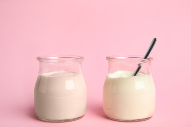 Photo of Tasty organic yogurt in glass jars on pink background