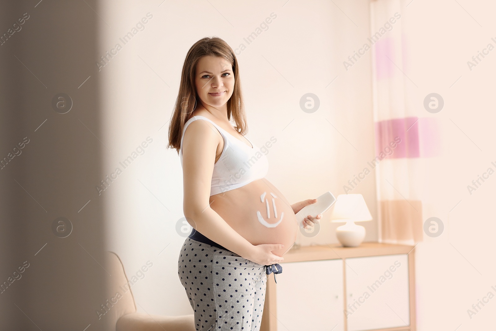 Photo of Pregnant woman with smile painted on her belly against blurred background