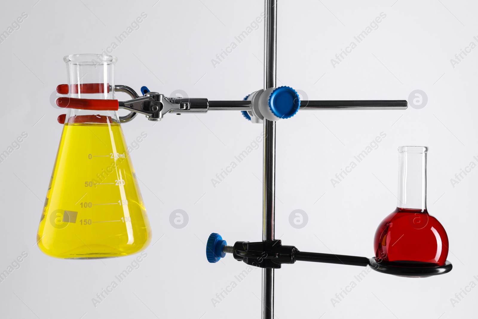 Photo of Retort stand and laboratory flasks with liquids on white background