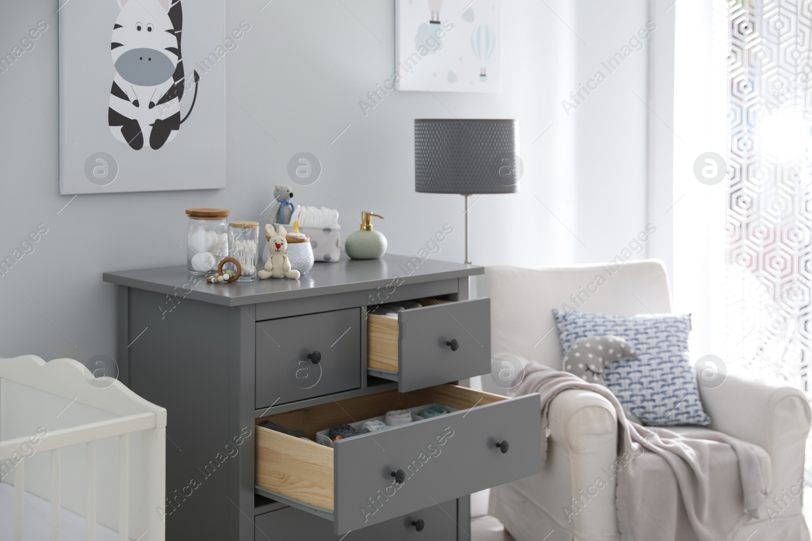 Photo of Modern open chest of drawers with baby clothes and accessories in room