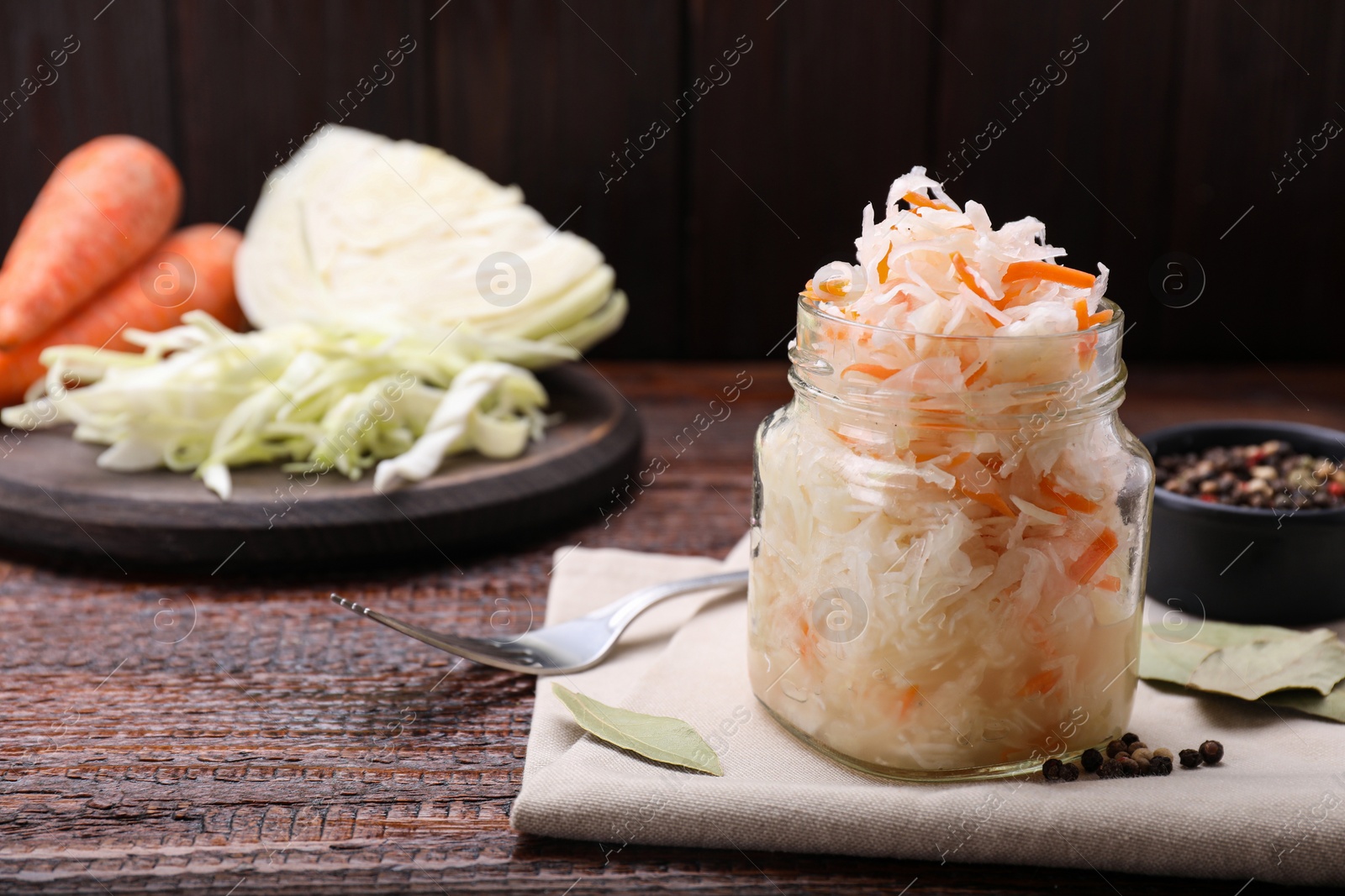 Photo of Glass jar of tasty sauerkraut on wooden table, space for text