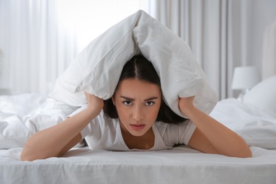 Photo of Unhappy young woman covering ears with pillow in bed at home. Noisy neighbours