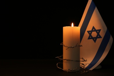 Photo of Flag of Israel, barbed wire and burning candle on black background, space for text. Holocaust memory day