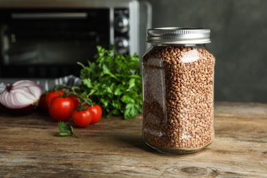 Buckwheat grains in jar on wooden table. Space for text