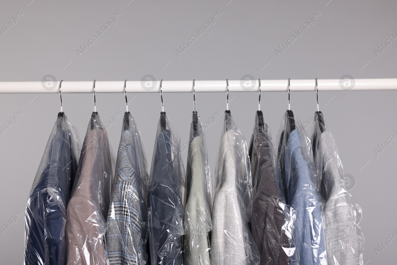 Photo of Dry-cleaning service. Many different clothes in plastic bags hanging on rack against grey background