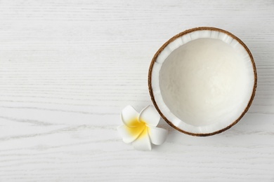 Photo of Half of coconut and flower on white wooden background, top view. Space for text