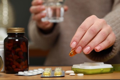 Woman taking pill from plastic box at wooden table indoors, closeup