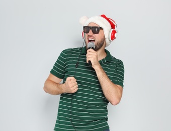 Photo of Young man in Santa hat singing into microphone on color background. Christmas music