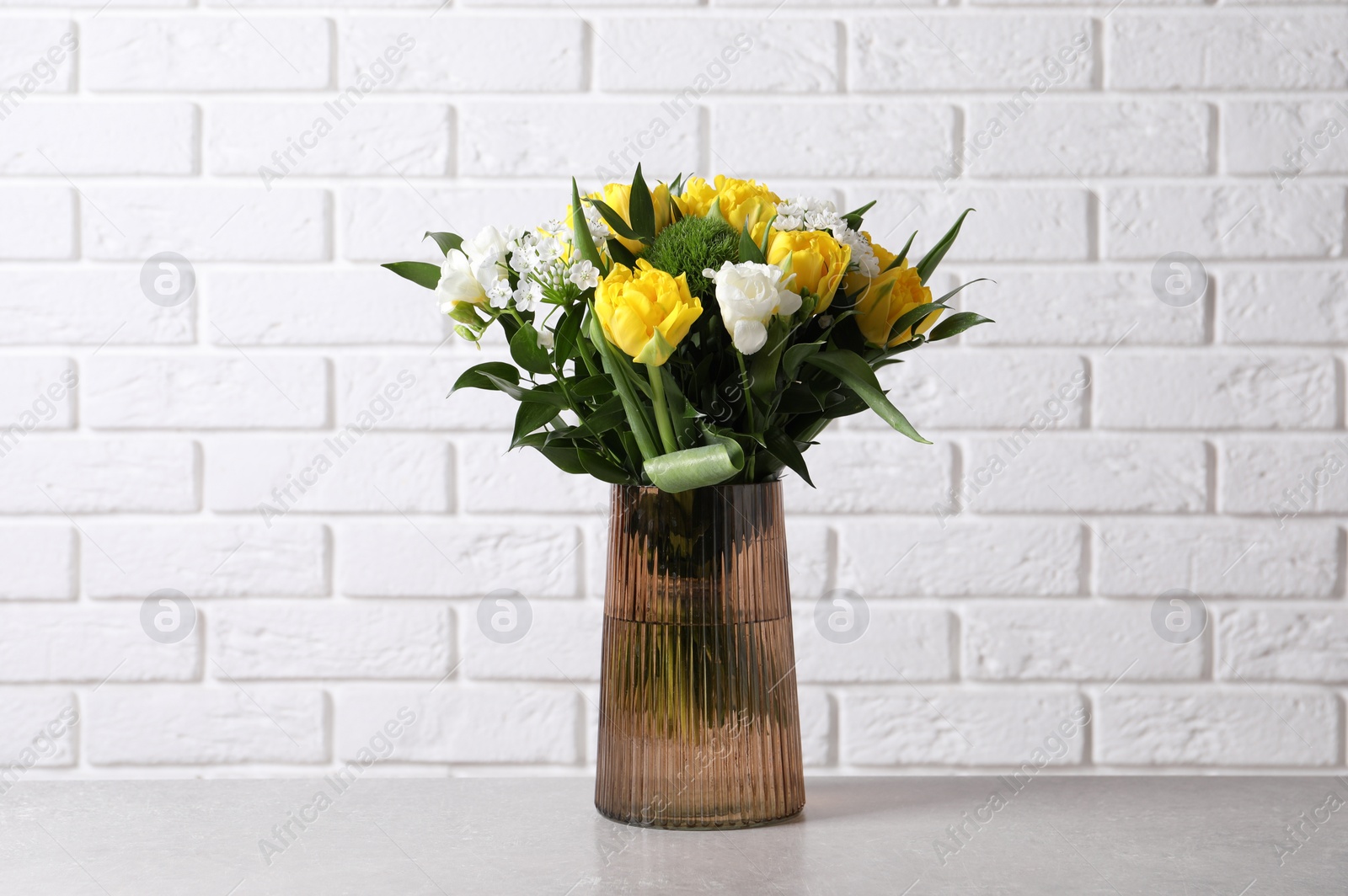 Photo of Beautiful bouquet with peony tulips on grey table near white brick wall