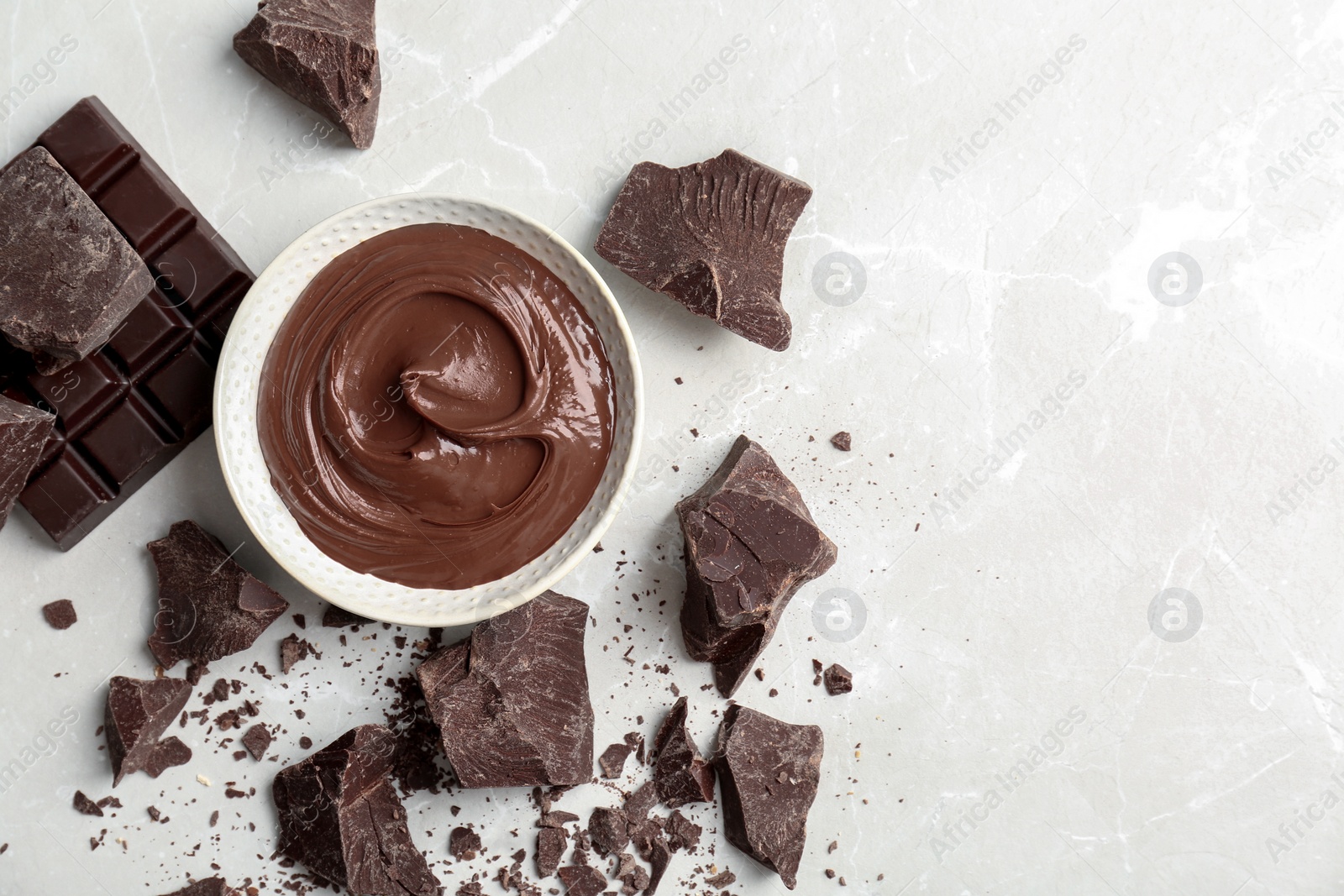 Photo of Bowl with tasty melted chocolate and pieces on table, top view