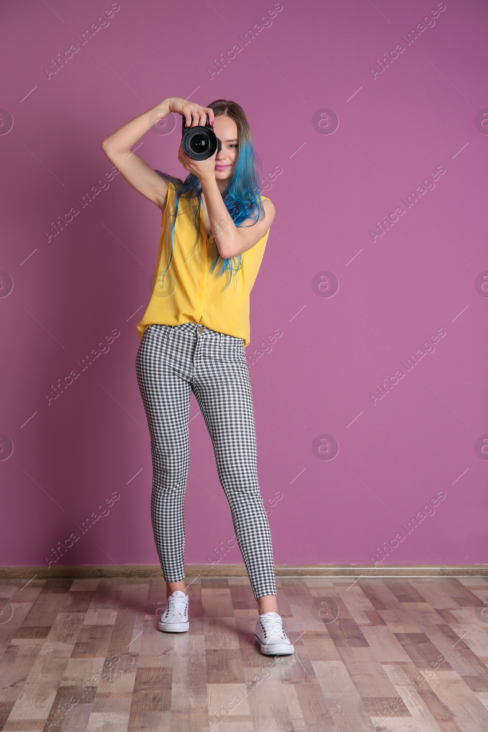 Photo of Young female photographer with camera near color wall