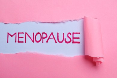 Photo of Word Menopause written on white background, view through hole in pink paper