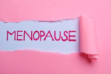 Word Menopause written on white background, view through hole in pink paper