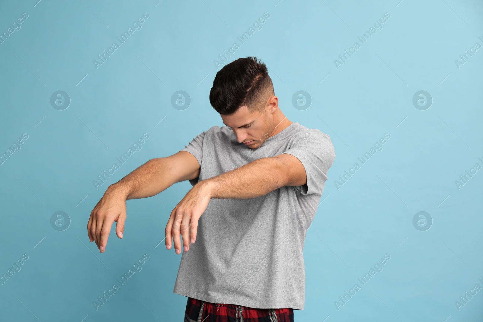 Photo of Somnambulist in pajamas on light blue background. Sleepwalking