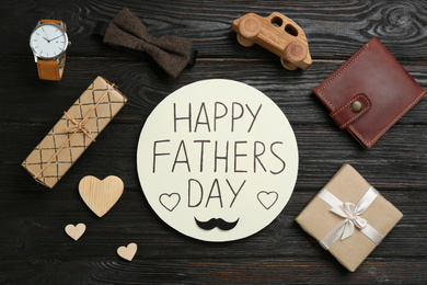 Photo of Card with phrase HAPPY FATHER'S DAY and male accessories on black wooden background, flat lay