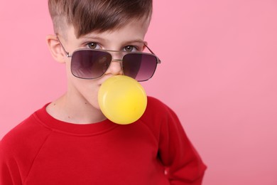 Photo of Boy in sunglasses blowing bubble gum on pink background, space for text