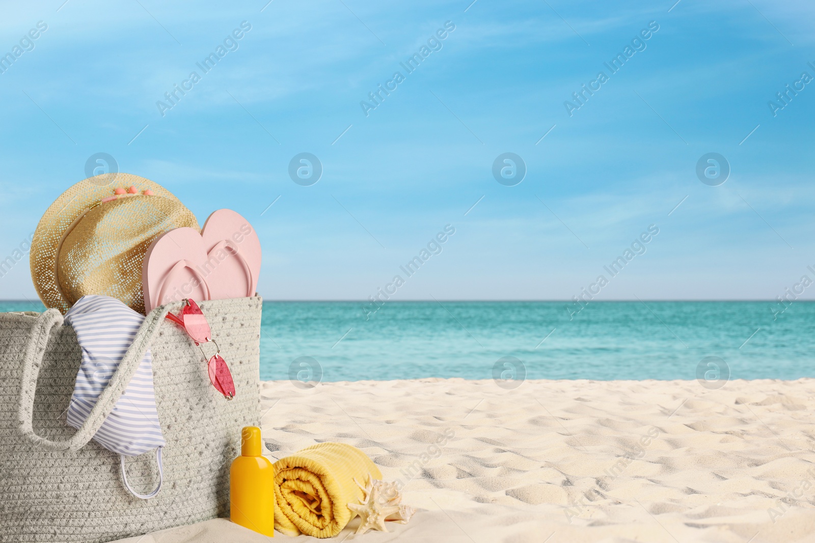 Image of Bag with bikini and accessories on sunny ocean beach, space for text. Summer vacation