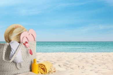 Bag with bikini and accessories on sunny ocean beach, space for text. Summer vacation