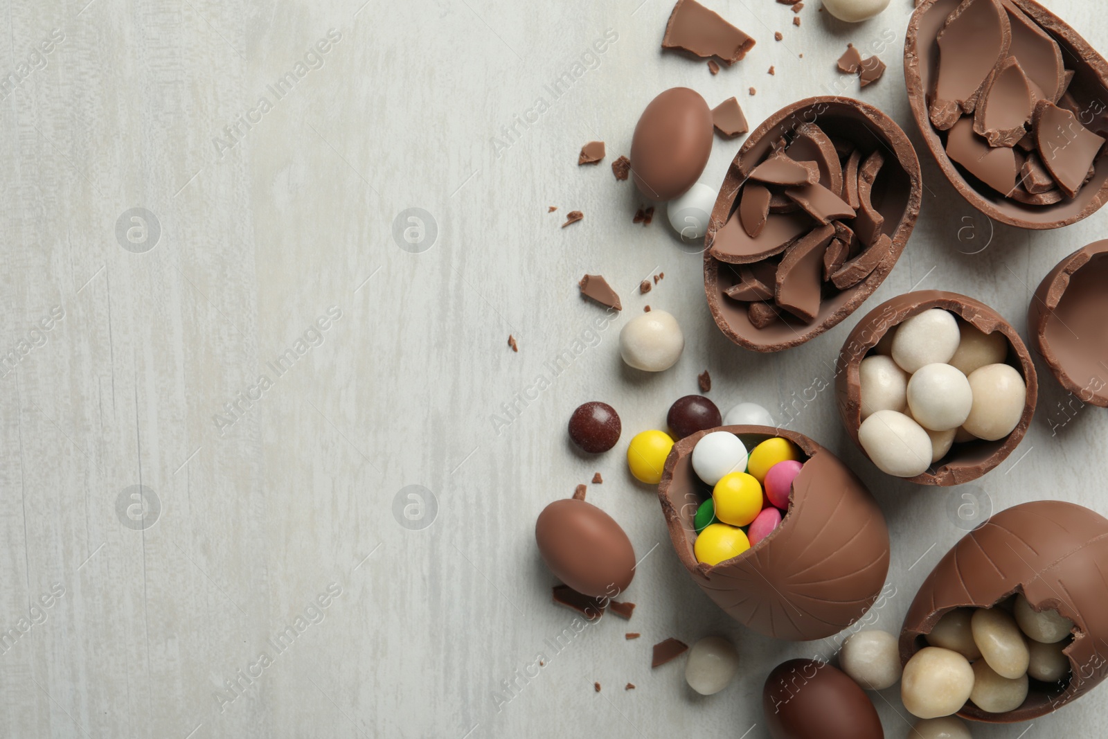 Photo of Broken chocolate eggs with candies on white wooden table, flat lay. Space for text