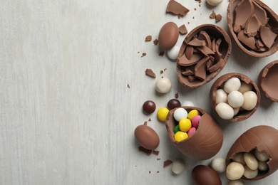 Photo of Broken chocolate eggs with candies on white wooden table, flat lay. Space for text